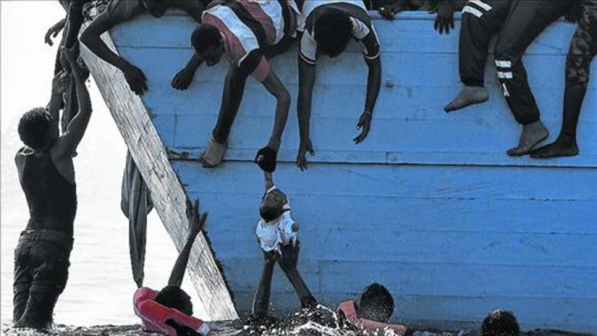Unos inmigrantes tratan de sacar a un niño del mar frente a las costas de Libia, en una foto de archivo.-ARIS MESSINIS