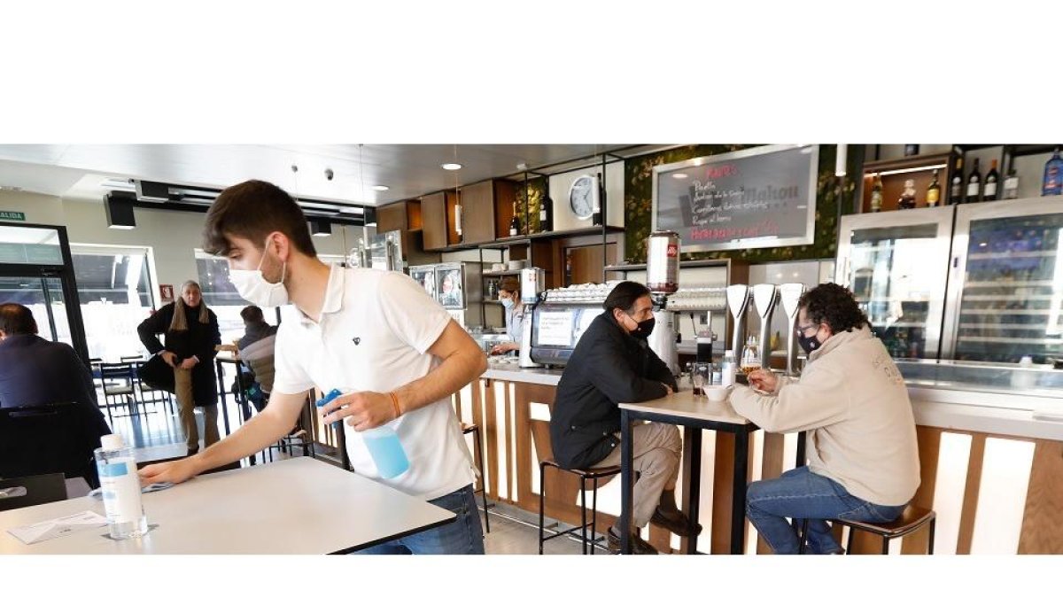 Un camarero desinfecta la mesa en el Café Villa de Prado el día antes del cierre del interior de la hostelería mientras unos clientes disfrutan de su consumición. / J.M. LOSTAU