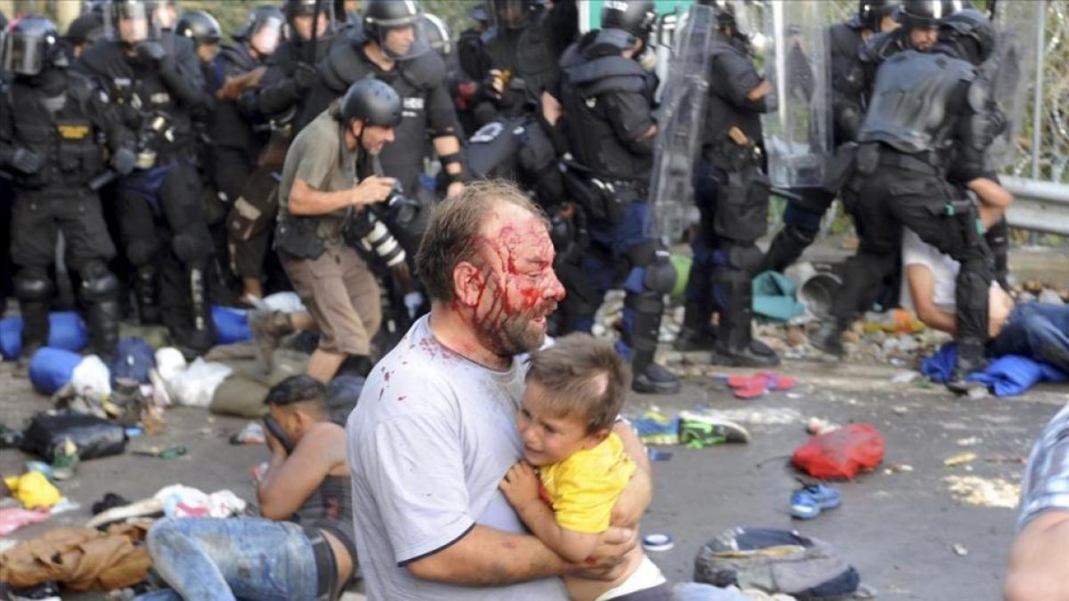 Un refugiado sirio con un niño en brazos en los disturbios de Röszke, en la frontera entre Serbia y Hungría en septiembre del 2015.-KARNOK CSABA