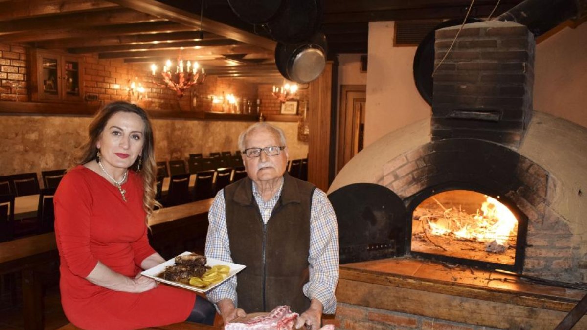 Olga y su padre, José Camarero, con un plato de carne estofada y el lechazo con IGP, junto al horno de asar del restaurante.-ARGICOMUNICACIÓN