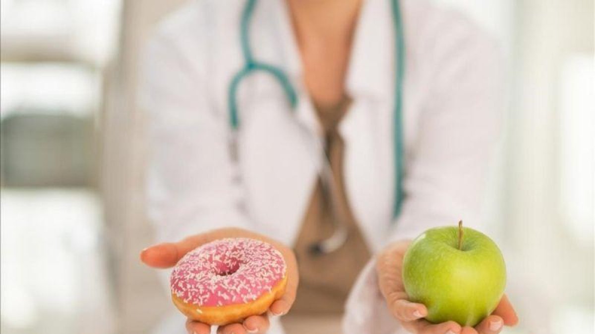 Una doctora dando a elegir entre un donut o una manzana.-123RF