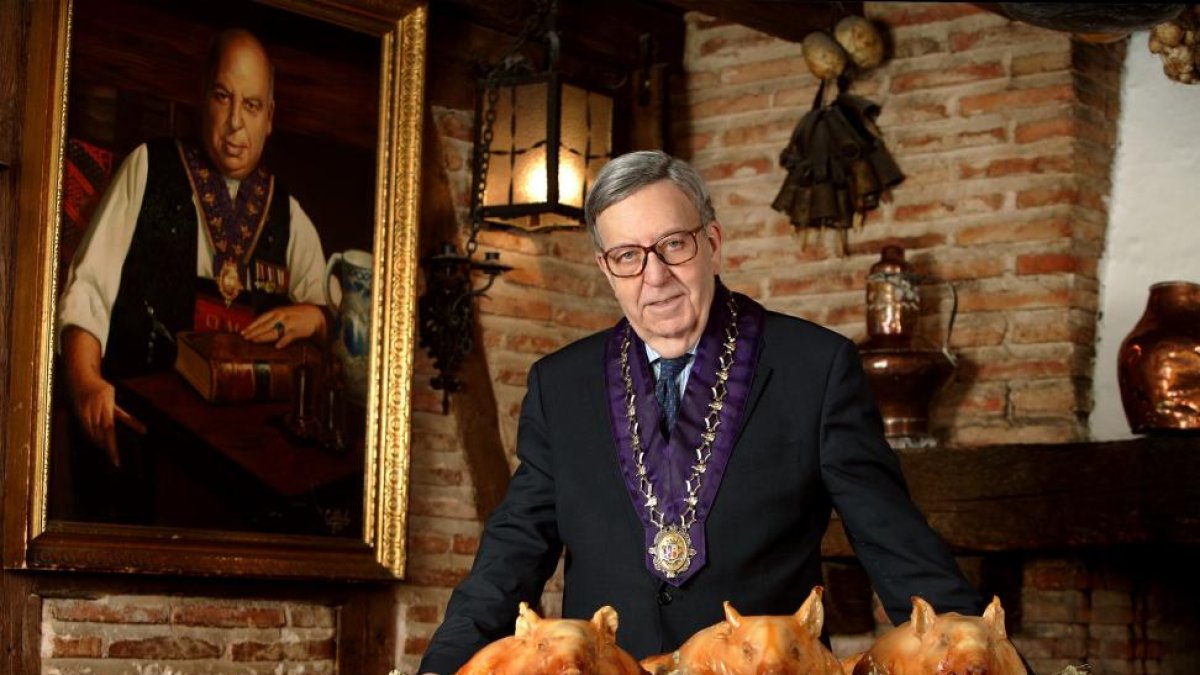 Alberto Cándido López, hijo del mesonero Cándido, con los cochinillos asados que han dado la vuelta al mundo, sobre las andas, y un retrato de su padre detrás, en el Mesón de Cándido de Segovia.-ARGICOMUNICACIÓN