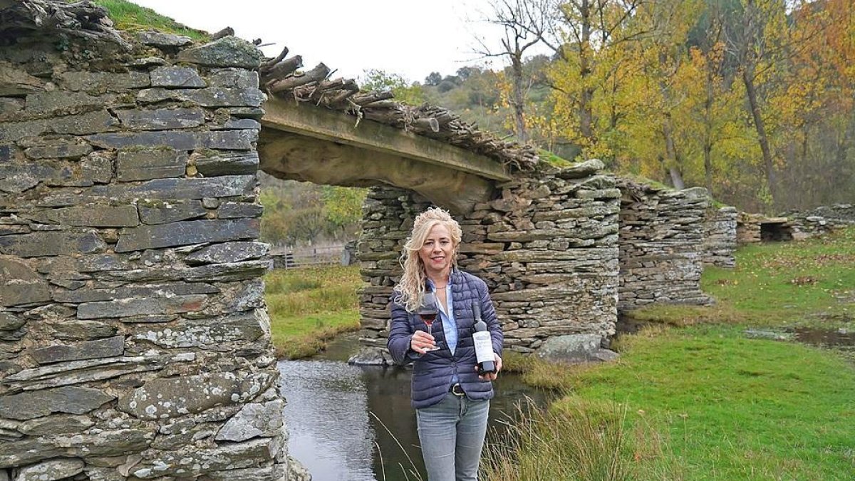 Teodora López posa con uno de sus vinos en la mano, frente a ‘la puente’ de su pueblo Fradellos de Aliste.-J. FERRERO