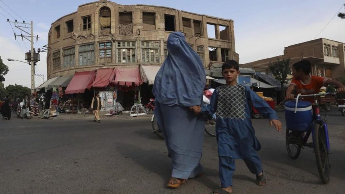 Una mujer afgana vestida con un burka agarra de la mano a su hijo al cruzar una calle en Herat, Afganistán, este jueves.-EFE / JALIL REZAYEE