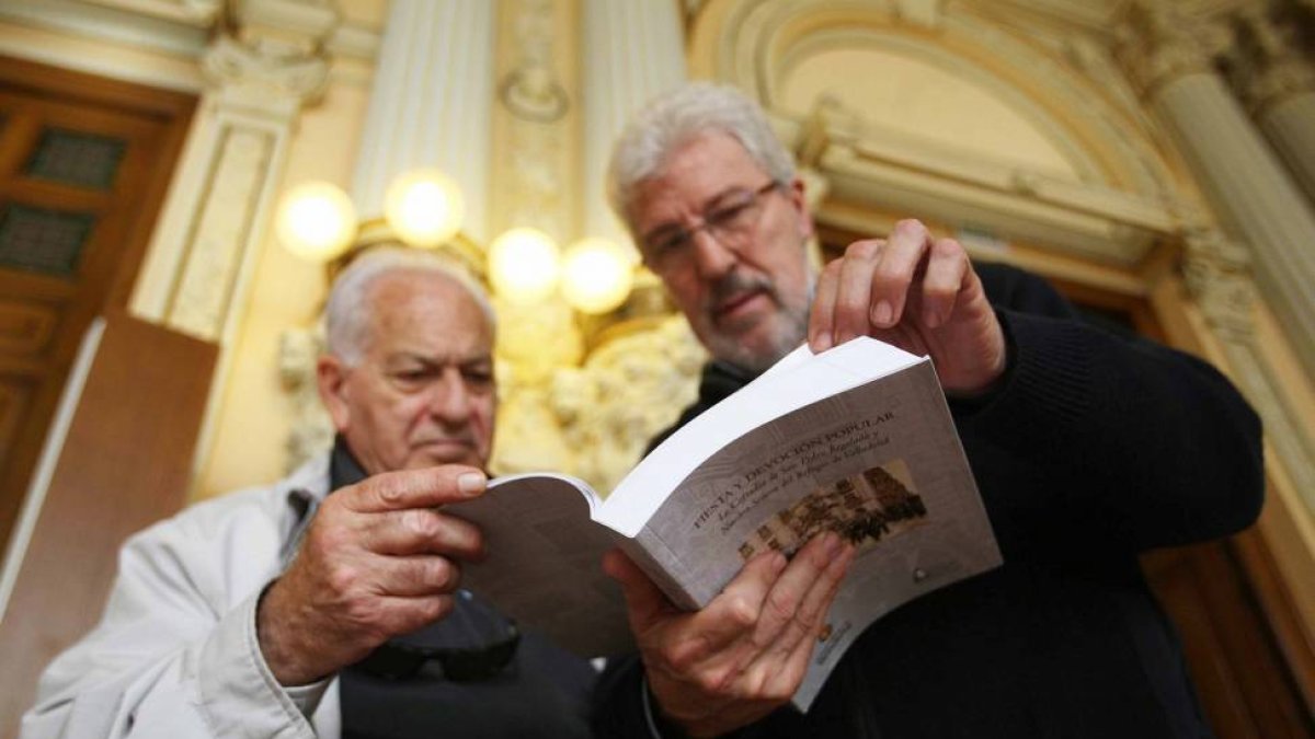 Dos asistentes a la presentación del libro 'Fiesta y devoción popular: la Cofradía de San Pedro Regalado y Nuestra Señora del Refugio de Valladolid', ojean el volumen-Ical