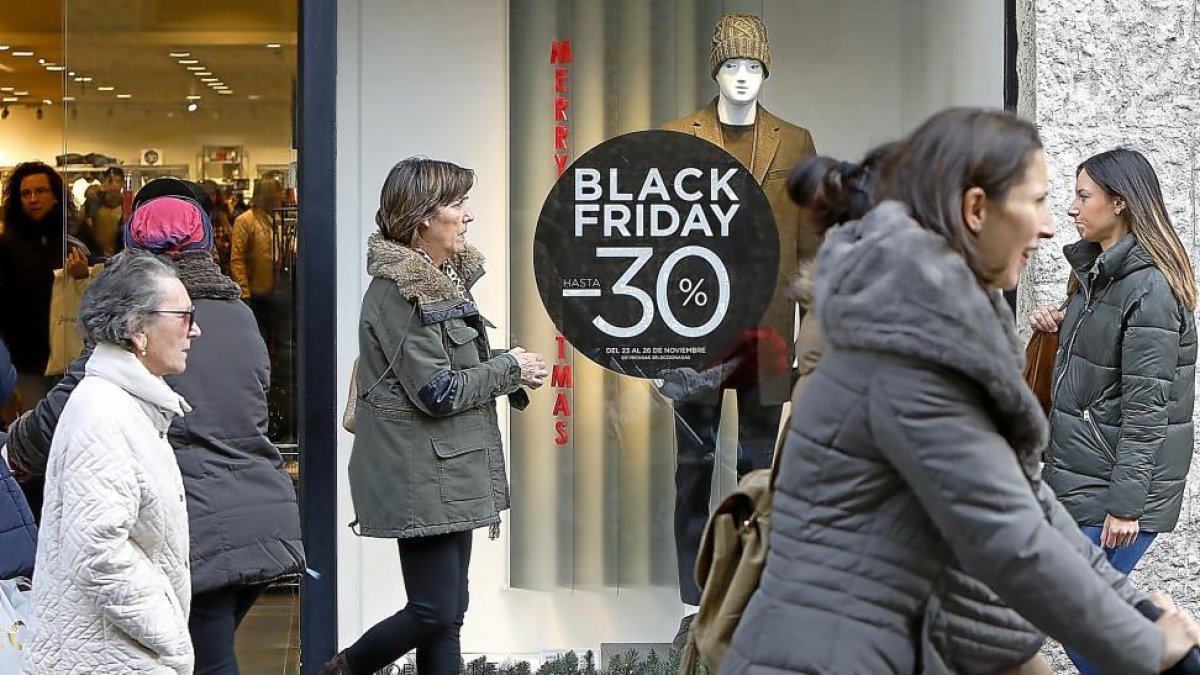 Transeúntes pasean por la calle Santiago de Valladolid ante un establecimiento de ropa con el cartel de descuento por el Blak Friday en el escaparate.-J.M. LOSTAU