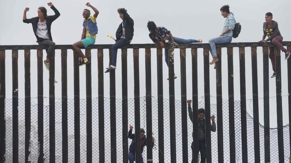 Miembros de la caravana de migrantes que cruzó México a pie hasta la frontera con Estados Unidos trepan el muro fronterizo que separa ambos países el pasado 29 de abril del 2018.-SANDY HUFFAKER (AFP)