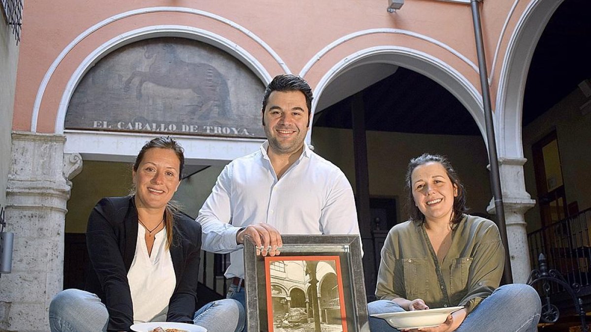 Sara, Santi y Macarena posan en el patio del restaurante con una fotografía tomada en el mismo lugar años atrás y dos de los platos de su carta-