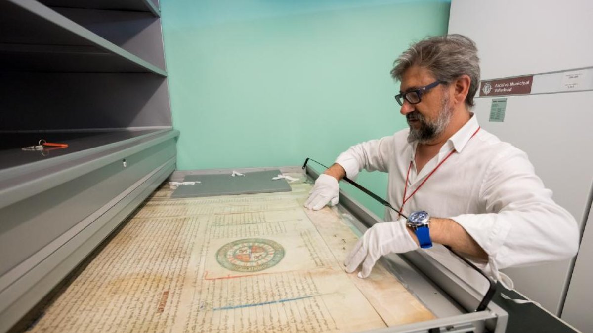 A la izquierda, imagen del documento más antiguo que se conserva. Arriba, el director del Archivo Municipal manipulando un pergamino medieval.-PABLO REQUEJO
