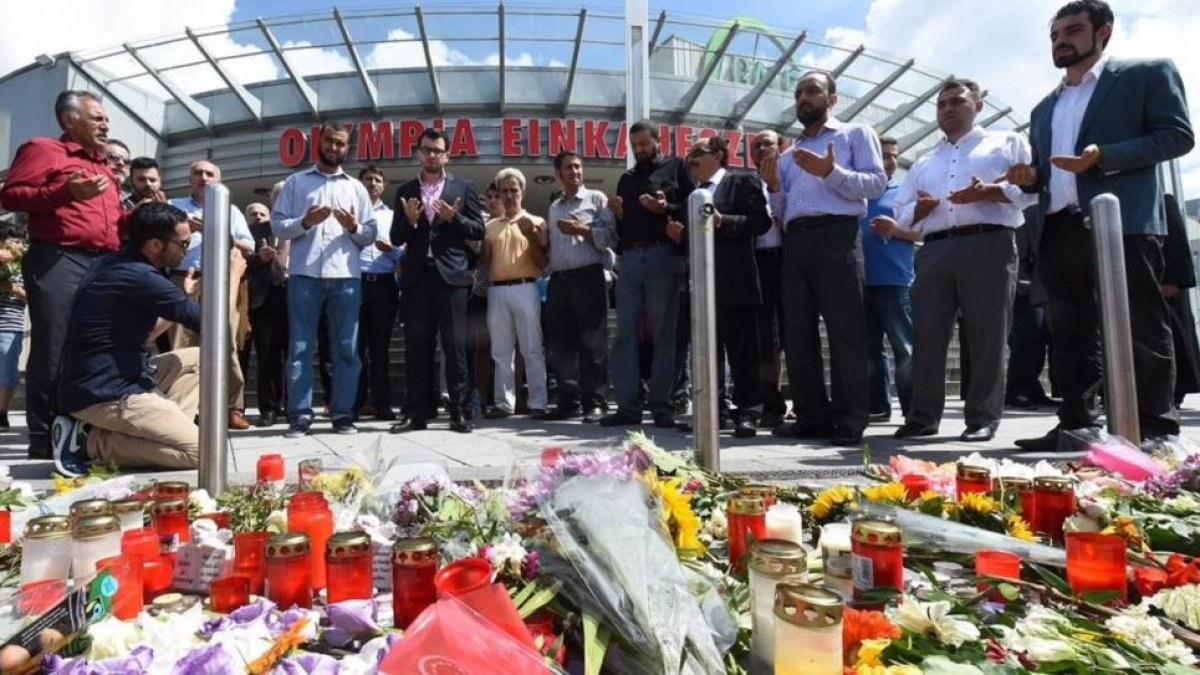 Varias personas rezan en el memorial de velas y flores, colocada frente al centro comercial Olympia, en Munich, este domingo.-AFP / CHRISTOF STACHE