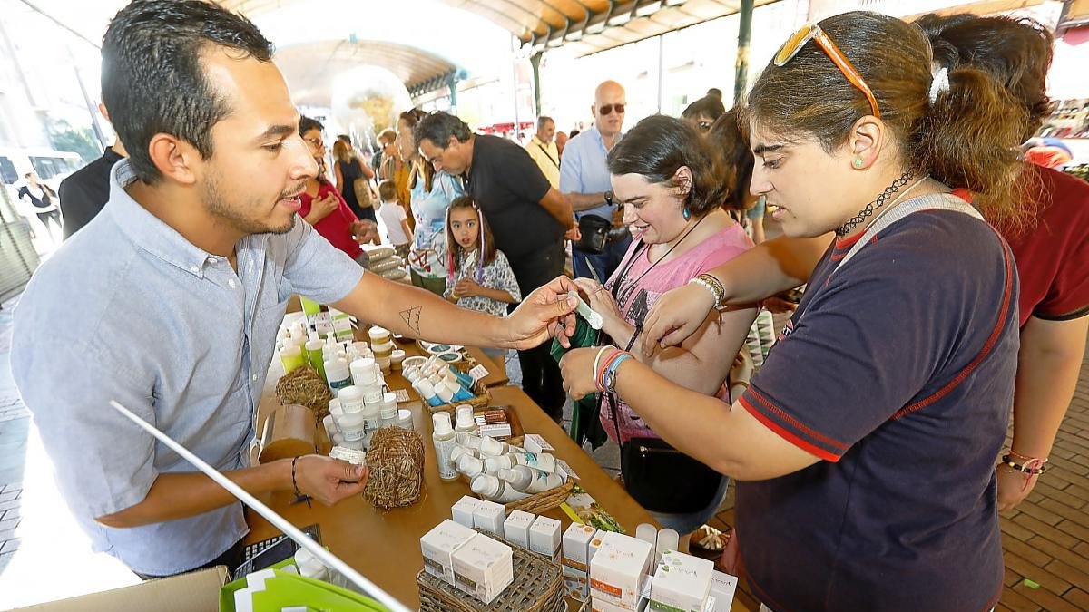 Un tendero da a probar uno de sus productos a un cliente en su puesto durante el primer Ecomercado.-J.M. LOSTAU