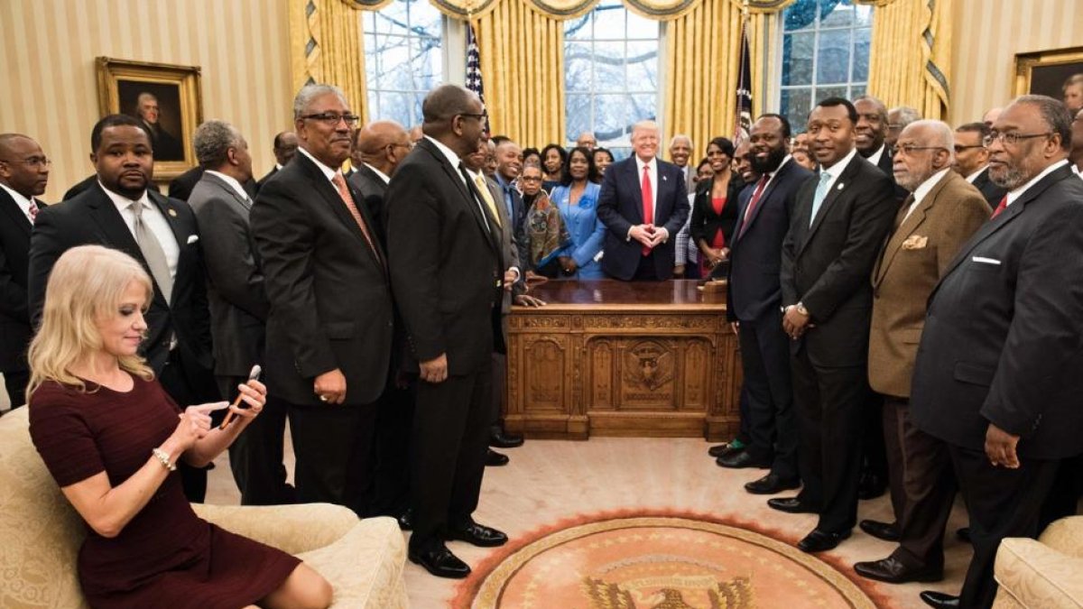 Kellyanne Conway, de rodillas y con zapatos, consulta su móvil mientras Trump y sus invitados posan para la foto oficial-AFP