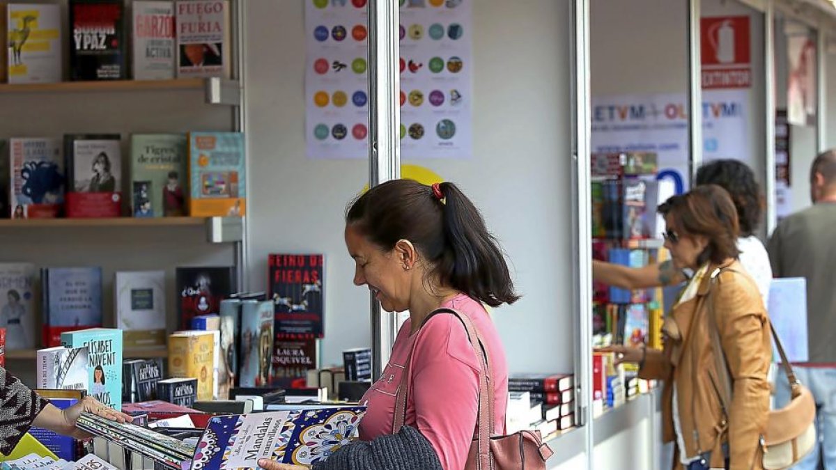 Una mujer observa un libro en una de las casetas de la feria.-ICAL