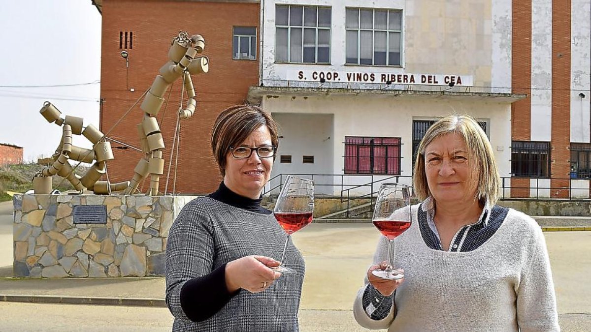 De izquierda a derecha, Marta Fernández y Mariló Maroto, con el rosado de la cooperativa, ante la escultura que rinde homenaje a los hombres y mujeres que construyeron las bodegas subterráneas de Valderas y plantaron sus viñas.-ARGI