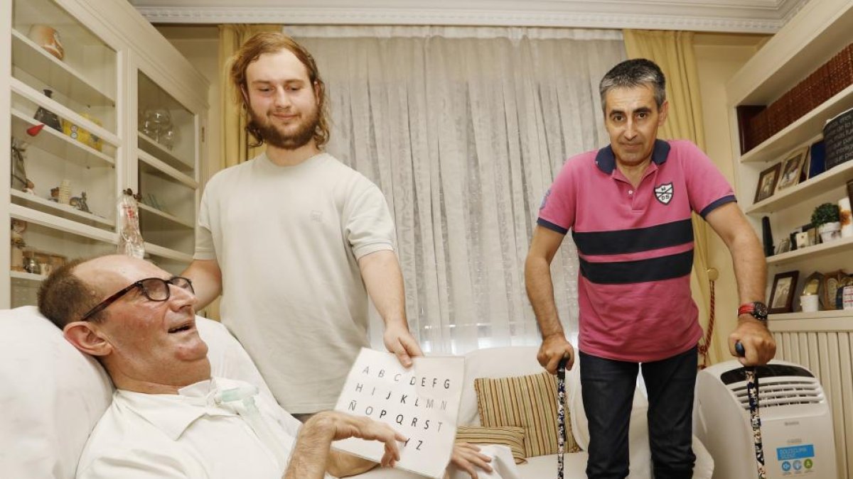Juan José Fonseca señala el abecedario con el que se expresa y su hijo Álvaro, en pie, le traduce. En el salón de los Fonseca también está otro paciente de ELA, José Antonio Francos, que necesita caminar con bastones por su enfermedad-J.M. LOSTAU
