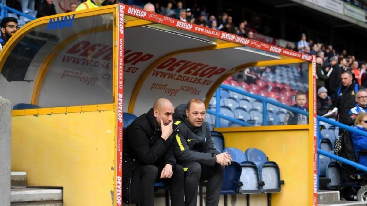 Guardiola charla con Rodolf Borrell, asistente suyo, en el banquillo del estadio del Huddersfield.-GETTY / LAURENCE GRIFFITHS