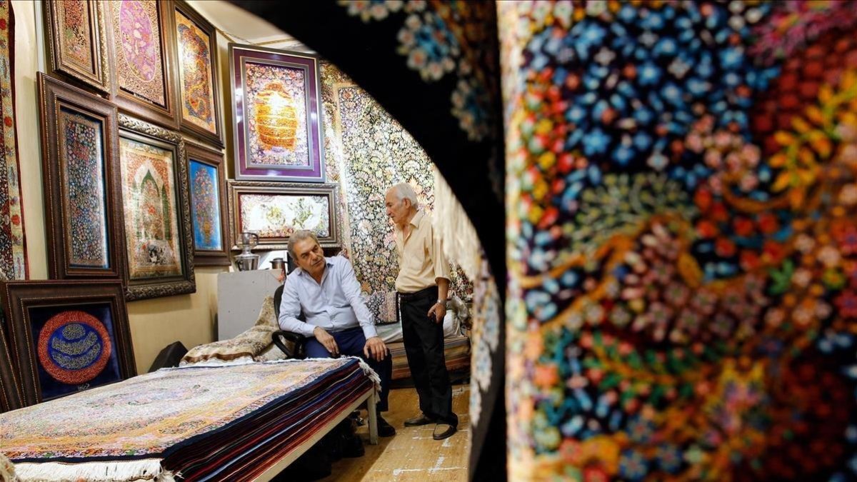 Dos hombres iranís conversan dentro de su negocio de alfombras en el Gran Bazar de Teherán. /-EFE / ABEDIN TAHERKENAREH