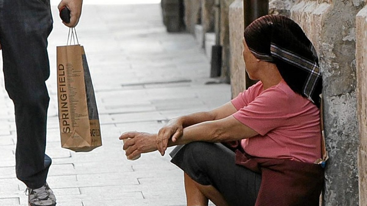 UNA PAREJA PASA JUNTO A UN POBRE QUE PIDE LIMOSNA CERCA DEL AYUNTAMIENTO DE VALLADOLID, EN LA IGLESÍA DE JESÚS NAZARENO. MENDICIDAD. POBREZA. HORIZONTAL
