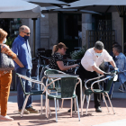 Un trabajador de una cafetería limpia las sillas mientras dos clientes esperan. J.M. LOSTAU