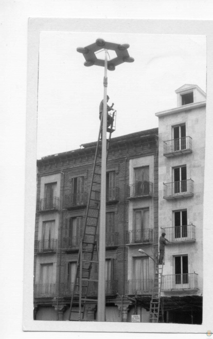 Un operario subido a una farola y otro instala cables en una fachada